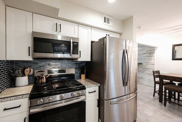 kitchen with white cabinets, stainless steel appliances, light tile patterned floors, and tasteful backsplash