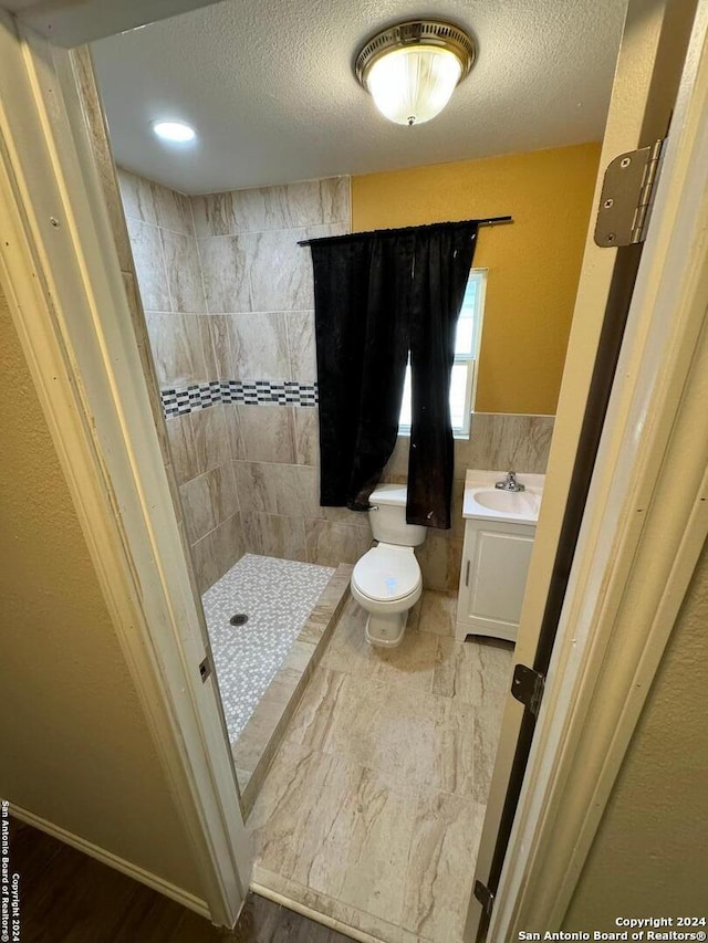 bathroom with a textured ceiling, toilet, tiled shower, vanity, and hardwood / wood-style flooring