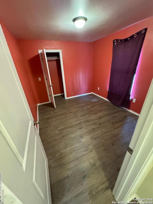 unfurnished bedroom featuring a textured ceiling, dark hardwood / wood-style floors, and a closet