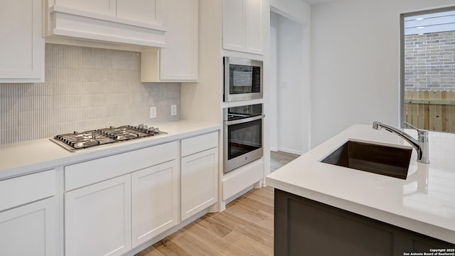 kitchen featuring stainless steel appliances, light countertops, custom range hood, white cabinetry, and a sink