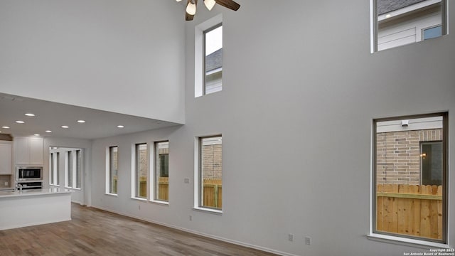 unfurnished living room featuring recessed lighting, a high ceiling, a ceiling fan, wood finished floors, and baseboards