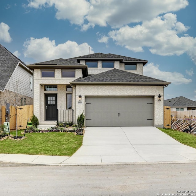 prairie-style home featuring a garage, brick siding, fence, concrete driveway, and a front yard