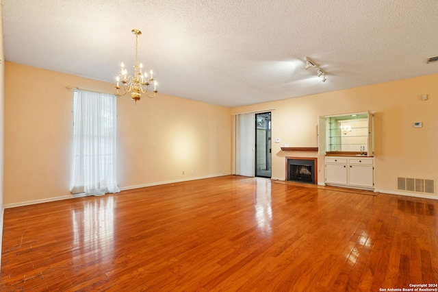 unfurnished living room featuring rail lighting, a notable chandelier, a textured ceiling, and light hardwood / wood-style floors