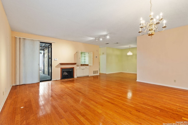 unfurnished living room with light hardwood / wood-style flooring, a textured ceiling, and a chandelier