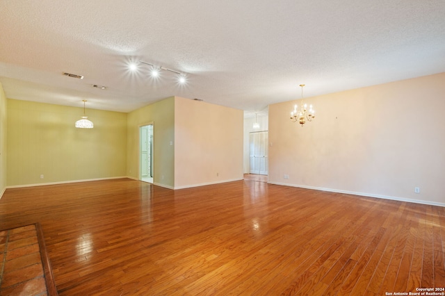 unfurnished room with hardwood / wood-style floors, a chandelier, and a textured ceiling