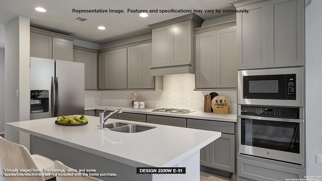 kitchen with light countertops, decorative backsplash, gray cabinets, appliances with stainless steel finishes, and a sink