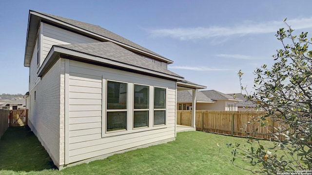 rear view of property featuring a lawn, a shingled roof, and fence