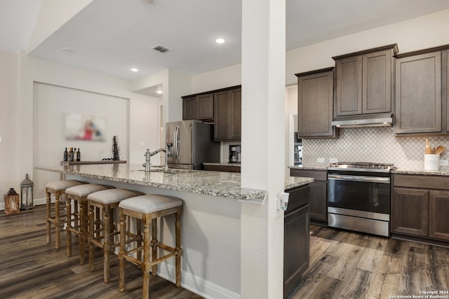 kitchen with tasteful backsplash, light stone countertops, dark hardwood / wood-style flooring, stainless steel appliances, and a breakfast bar area