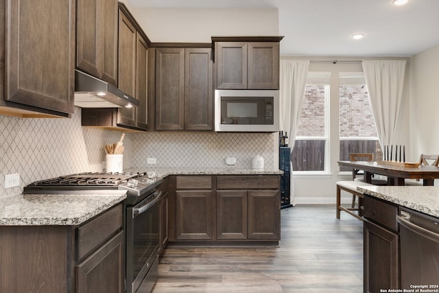 kitchen with ventilation hood, appliances with stainless steel finishes, dark brown cabinets, and wood-type flooring