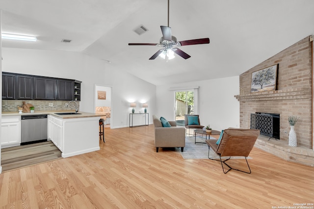 living room featuring sink, a fireplace, ceiling fan, high vaulted ceiling, and light hardwood / wood-style flooring