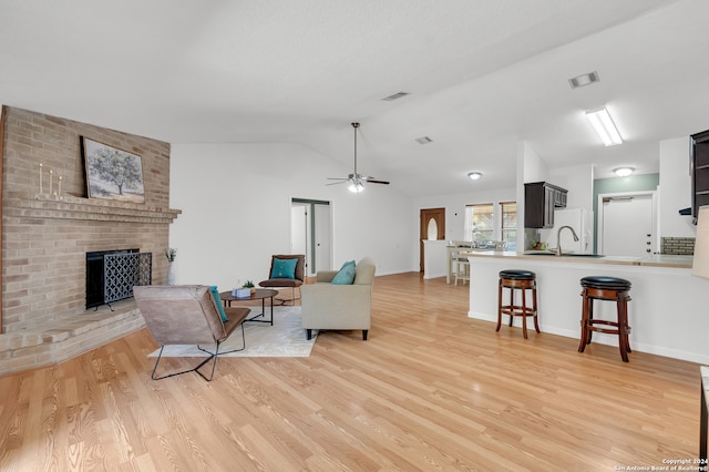 living room with ceiling fan, a brick fireplace, vaulted ceiling, light hardwood / wood-style flooring, and sink