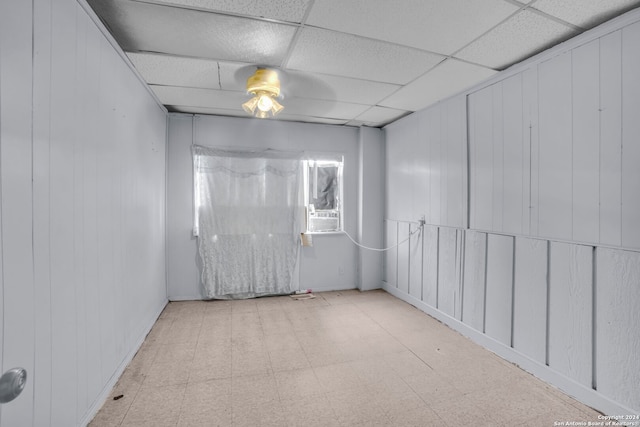 empty room with a drop ceiling, wooden walls, and ceiling fan