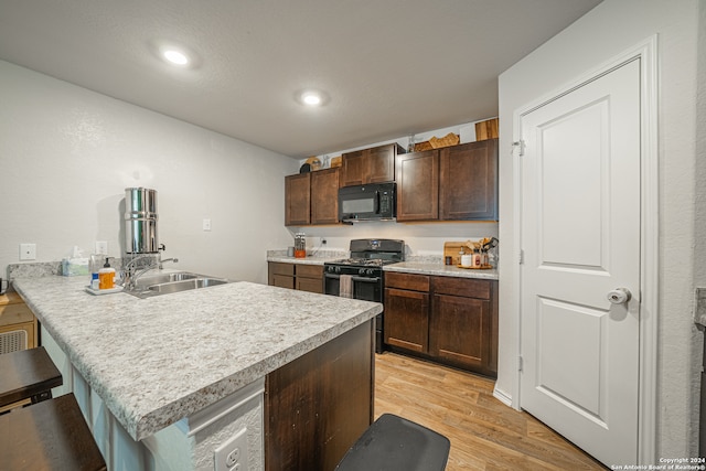 kitchen featuring black appliances, kitchen peninsula, light hardwood / wood-style floors, dark brown cabinetry, and a breakfast bar