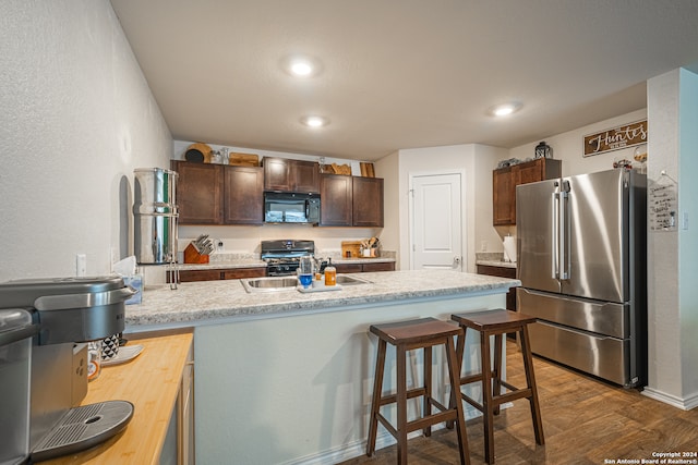 kitchen featuring hardwood / wood-style floors, dark brown cabinets, a breakfast bar, black appliances, and sink