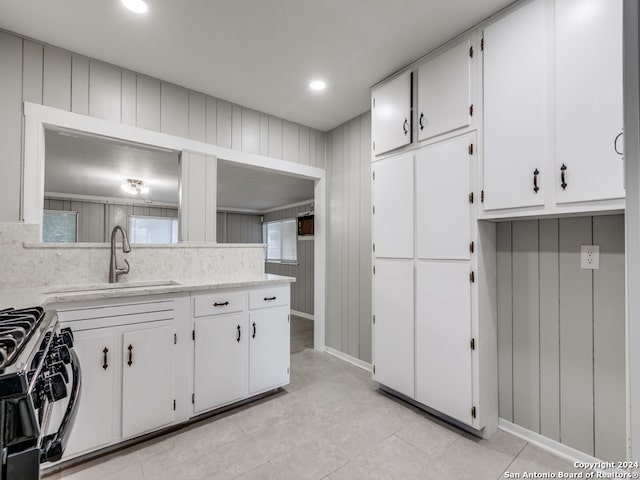 kitchen with gas range, light tile patterned flooring, white cabinets, and sink