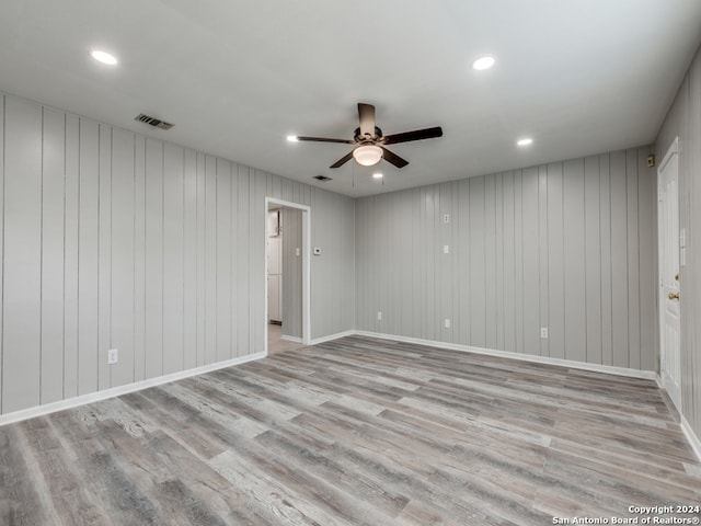 spare room with wood walls, light wood-type flooring, and ceiling fan