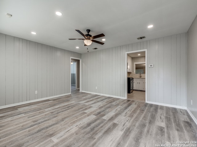 unfurnished room with ceiling fan, light hardwood / wood-style flooring, and wooden walls