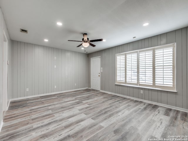 empty room with wooden walls, light hardwood / wood-style flooring, and ceiling fan