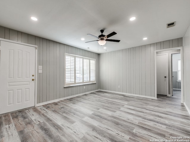 interior space featuring light hardwood / wood-style floors, wood walls, and ceiling fan