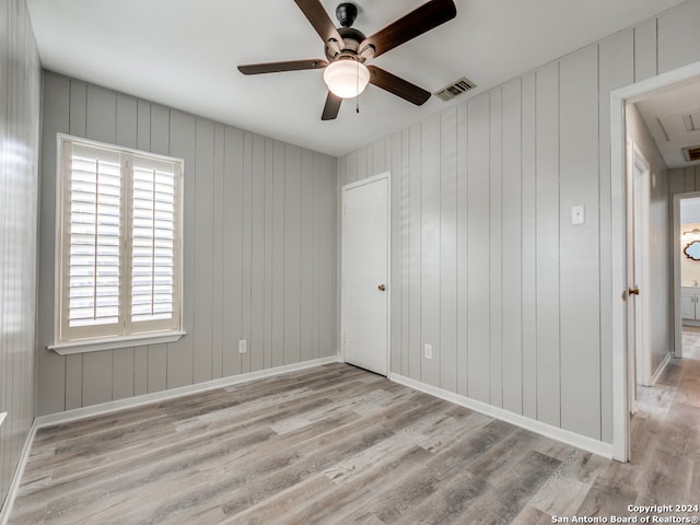 unfurnished room featuring ceiling fan, wood walls, and light wood-type flooring