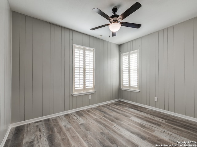 unfurnished room featuring wood walls, hardwood / wood-style flooring, and ceiling fan