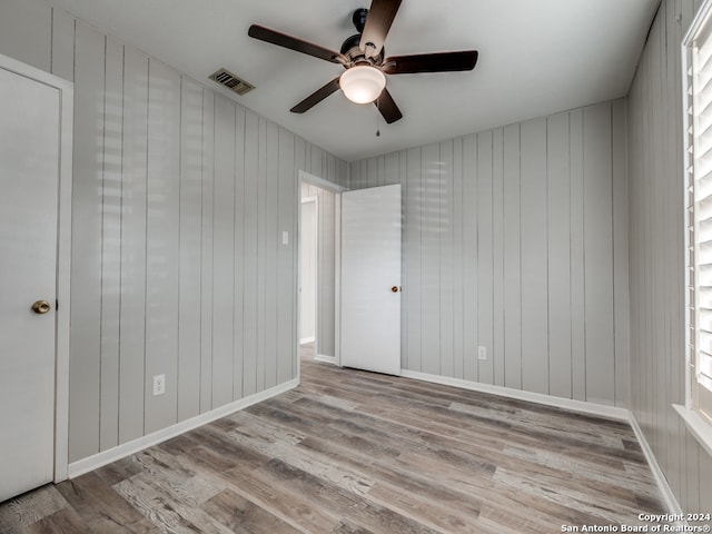 interior space with wood walls, light wood-type flooring, and ceiling fan