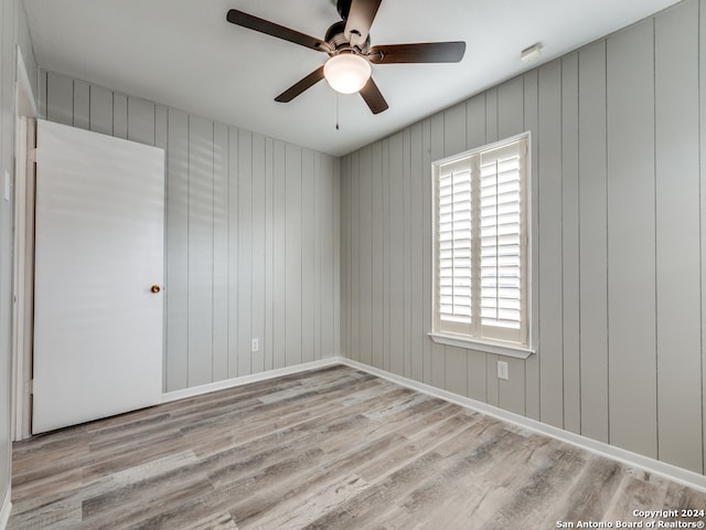 unfurnished room featuring wooden walls, light wood-type flooring, and ceiling fan