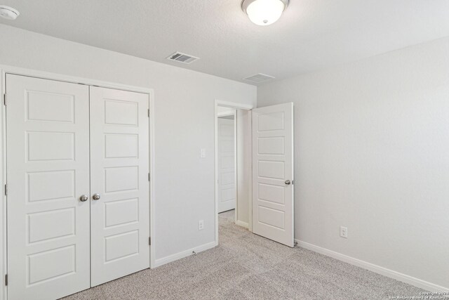 unfurnished bedroom with light colored carpet and a closet