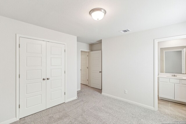 unfurnished bedroom featuring ensuite bathroom, a closet, light colored carpet, and sink