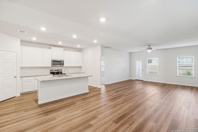 kitchen with light stone counters, stainless steel appliances, a center island with sink, light hardwood / wood-style floors, and white cabinetry