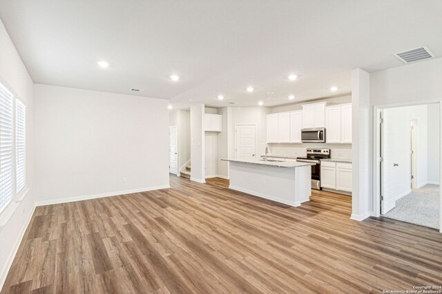 kitchen featuring light stone countertops, light wood-type flooring, stainless steel appliances, a kitchen island with sink, and white cabinets