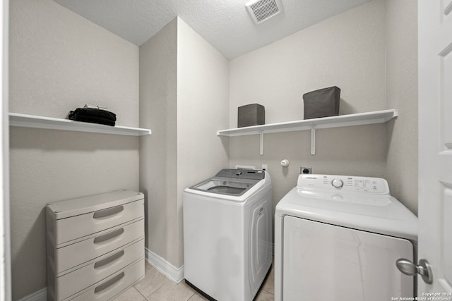 washroom featuring a textured ceiling, washing machine and dryer, and light tile patterned floors