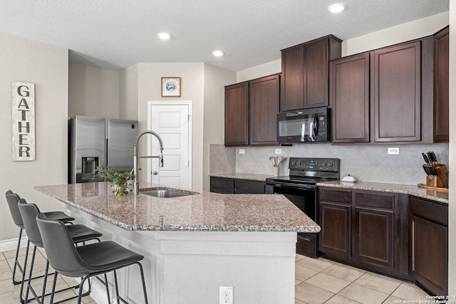 kitchen featuring black appliances, sink, a textured ceiling, a breakfast bar, and a kitchen island with sink