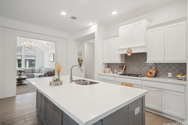 kitchen featuring white cabinets, stainless steel gas stovetop, sink, and a kitchen island with sink