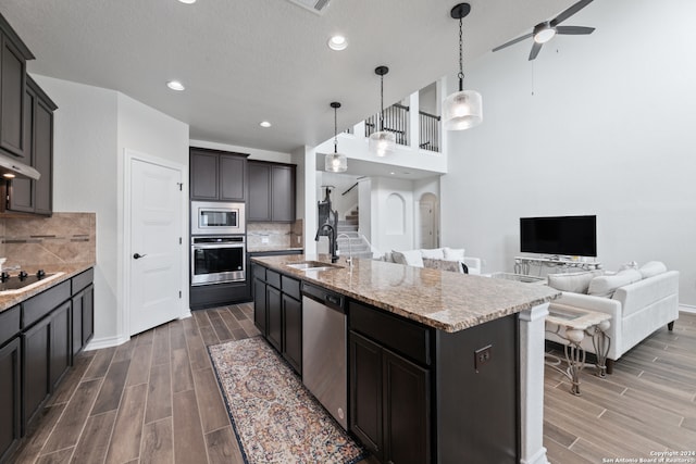 kitchen with appliances with stainless steel finishes, sink, hardwood / wood-style flooring, decorative backsplash, and a kitchen island with sink