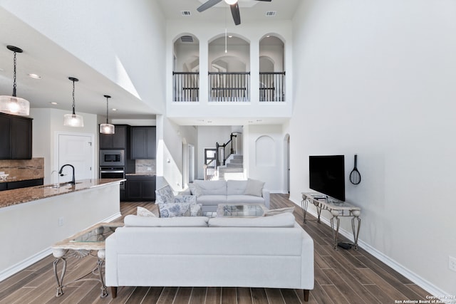 living room featuring ceiling fan, a towering ceiling, sink, and dark hardwood / wood-style floors