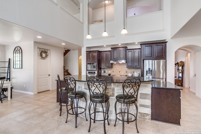 kitchen with a breakfast bar area, dark brown cabinets, stainless steel appliances, a center island with sink, and pendant lighting