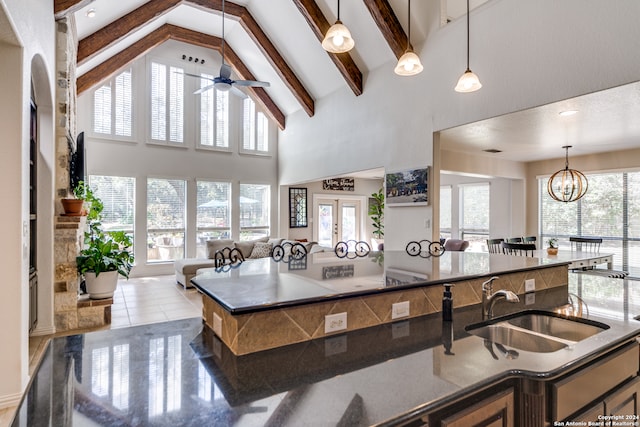 kitchen featuring beam ceiling, a center island with sink, sink, pendant lighting, and ceiling fan with notable chandelier