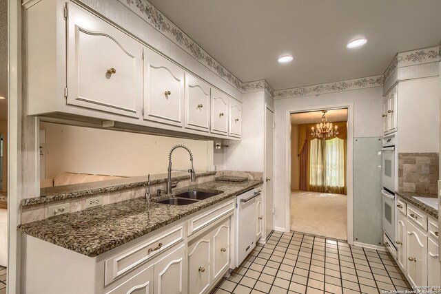 kitchen with sink, a notable chandelier, light colored carpet, white cabinetry, and white appliances