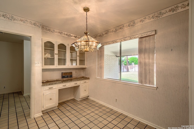 kitchen with built in desk, light stone countertops, light tile patterned flooring, pendant lighting, and white cabinetry