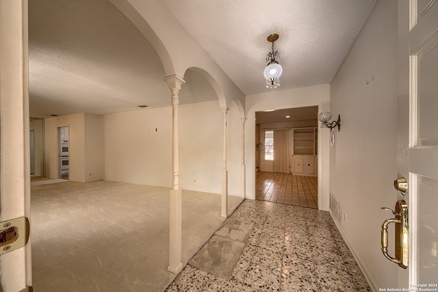 entryway with decorative columns, a textured ceiling, and vaulted ceiling