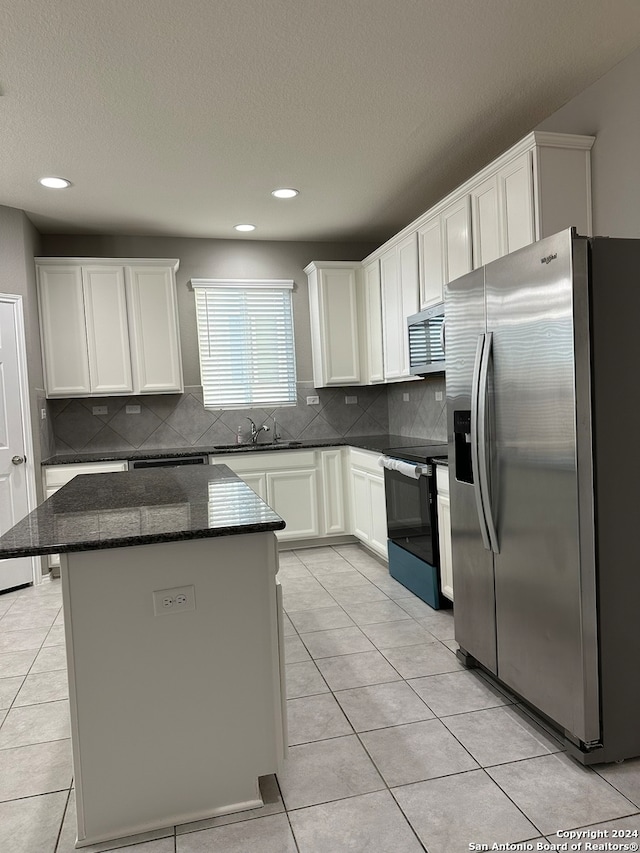 kitchen with light tile patterned flooring, a center island, stainless steel appliances, white cabinets, and dark stone countertops