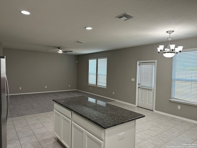 kitchen with white cabinets, hanging light fixtures, dark stone counters, ceiling fan with notable chandelier, and a center island