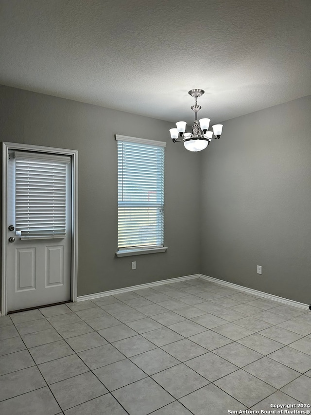 tiled empty room with a notable chandelier and a textured ceiling