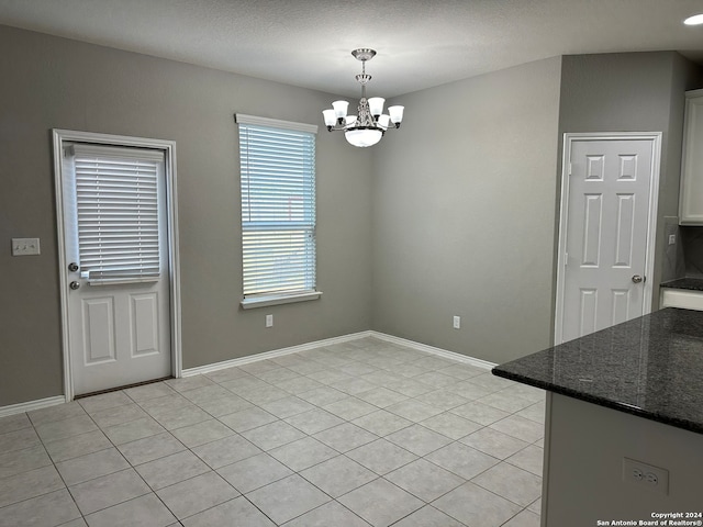 unfurnished dining area with light tile patterned floors, a textured ceiling, and an inviting chandelier