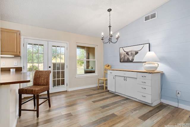 dining room featuring french doors, light wood-type flooring, a textured ceiling, a chandelier, and lofted ceiling