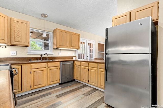 kitchen featuring sink, pendant lighting, a textured ceiling, appliances with stainless steel finishes, and light wood-type flooring