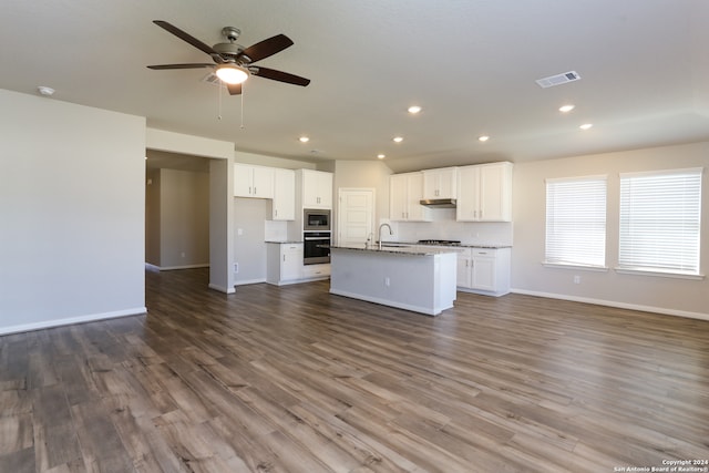 kitchen featuring white cabinets, hardwood / wood-style floors, an island with sink, appliances with stainless steel finishes, and dark stone countertops