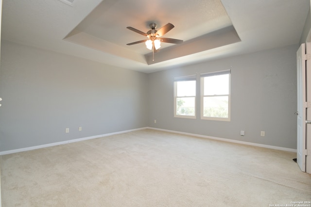 spare room featuring light colored carpet, a tray ceiling, and ceiling fan