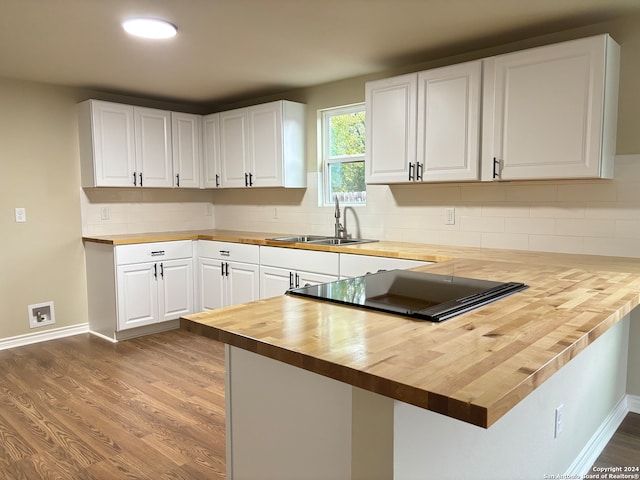 kitchen featuring light hardwood / wood-style flooring, kitchen peninsula, wood counters, sink, and white cabinets